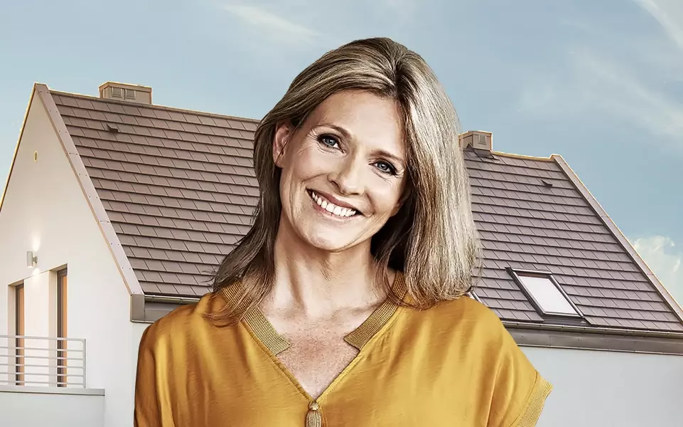 lächelnde Frau mit leicht schräg geneigtem Kopf steht vor modernem Einfamilienhaus